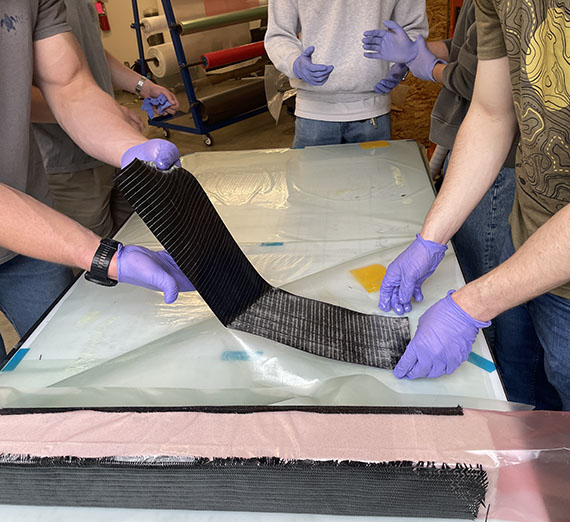 Two students wearing latex gloves hold a strip of wet carbon fiber