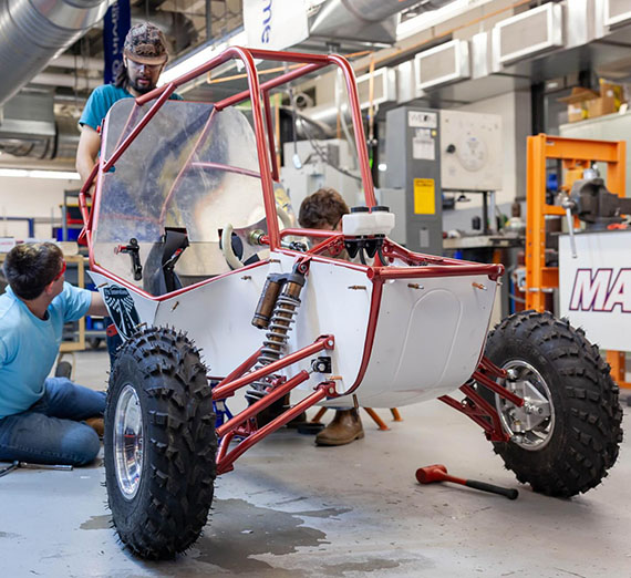 Three students sit next to a small, single-person off-road car