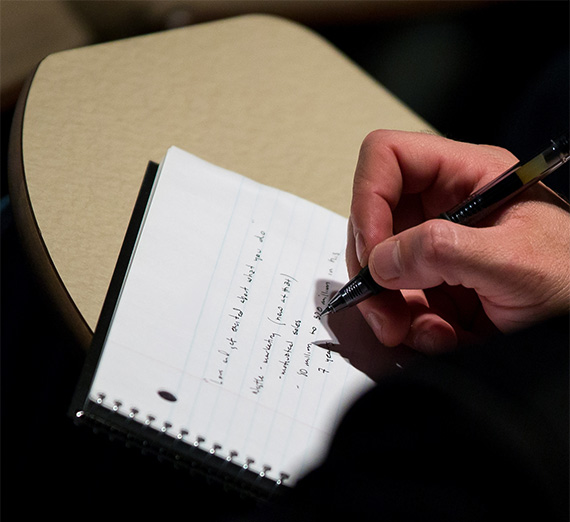 Close up of hand with a pen writing on white line paper.
