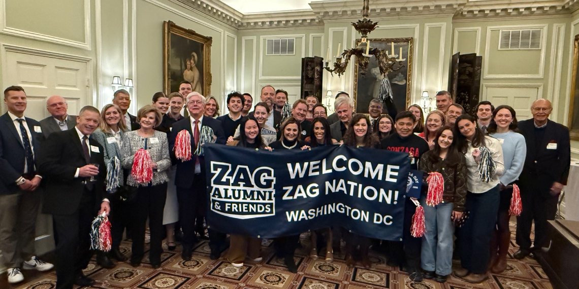 Attendees of the Forging Forward Washington, D.C. presidential event hold up a banner that with the Zag Alumni & Friends logo and text "Welcome Zag Nation! Washington D.C."