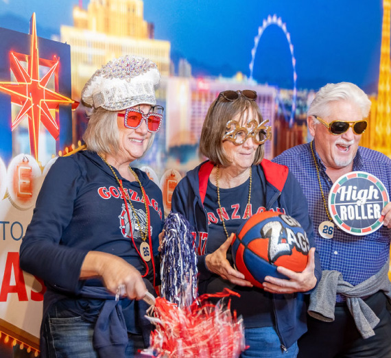 Attendees of the ZagUp event at the WCC Basketball Tournament in Las Vegas pose with props in front of  a Vegas-themed background.