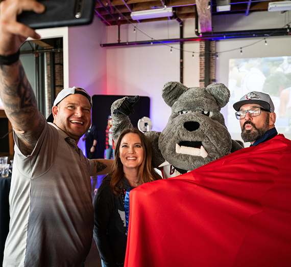 Gonzaga athletics mascot, Spike, and three alumni pose for a selfie at an event