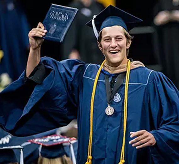 Graduating student smiling and holding a diploma folder.