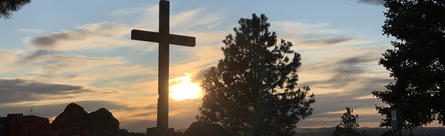 Cross sitting on a hill with a sunset