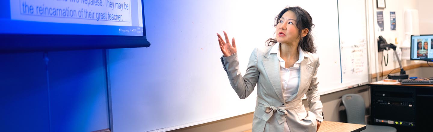 Female college teacher pointing at projector screen in classroom