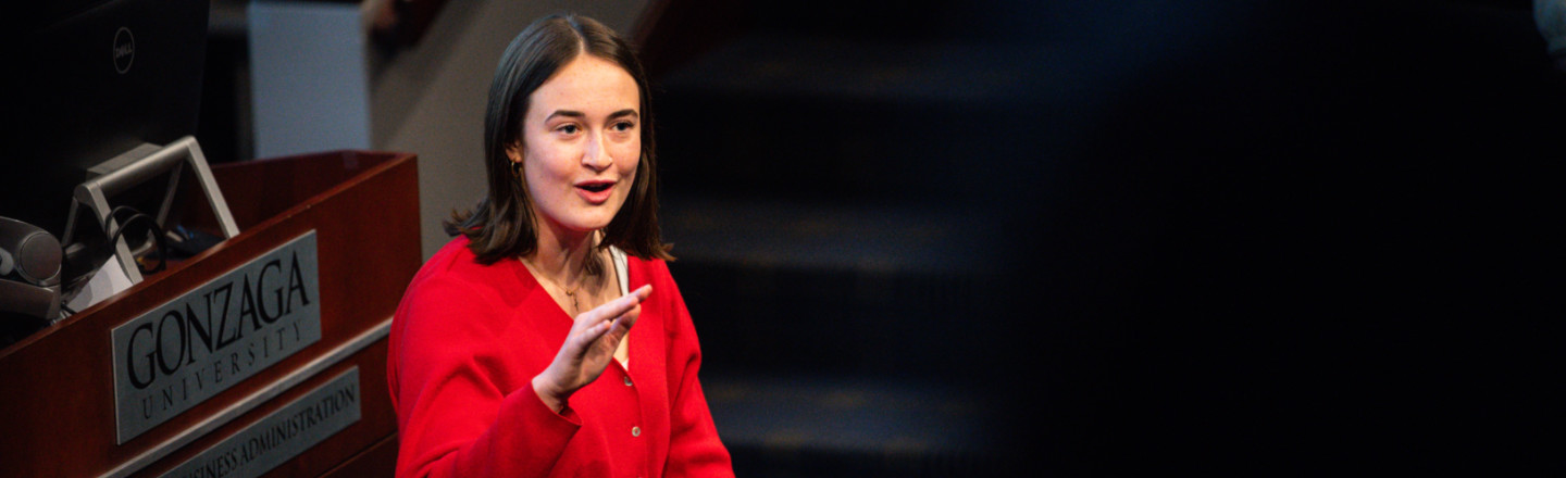 A speaker in a red shirt gesturing and talking.