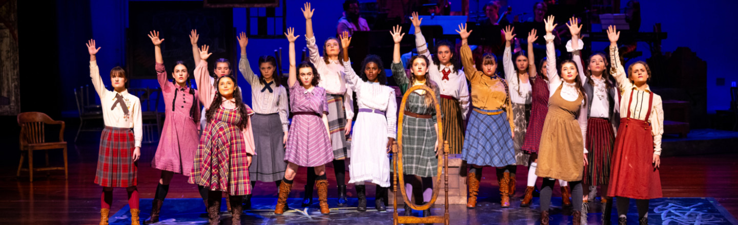Actors on stage in old fashioned clothes in a row raising hands in a Gonzaga Theatre, Music, and Dance production in the Myrtle Woldson Performing Arts Center.