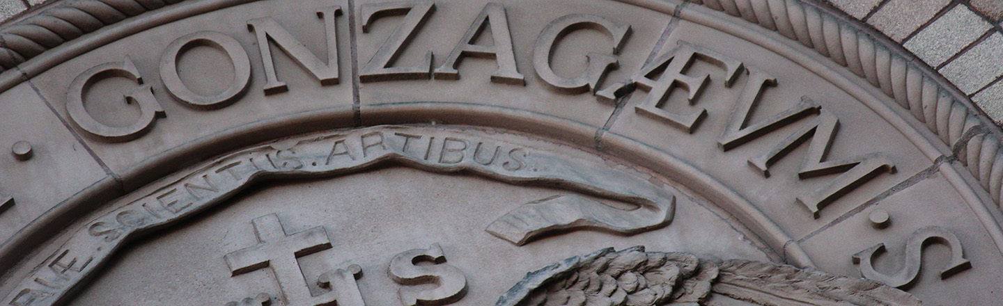 Metal casting of Gonzaga written in latin. Partial image of larger round casting set on side of a building.