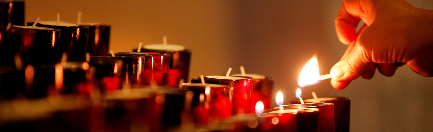 Close up of prayer candles being lit by hand.