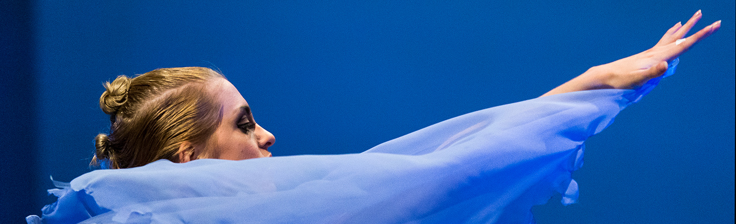 Close up side profile of female dancer facing right with arm and fingertips extended straight ahead.