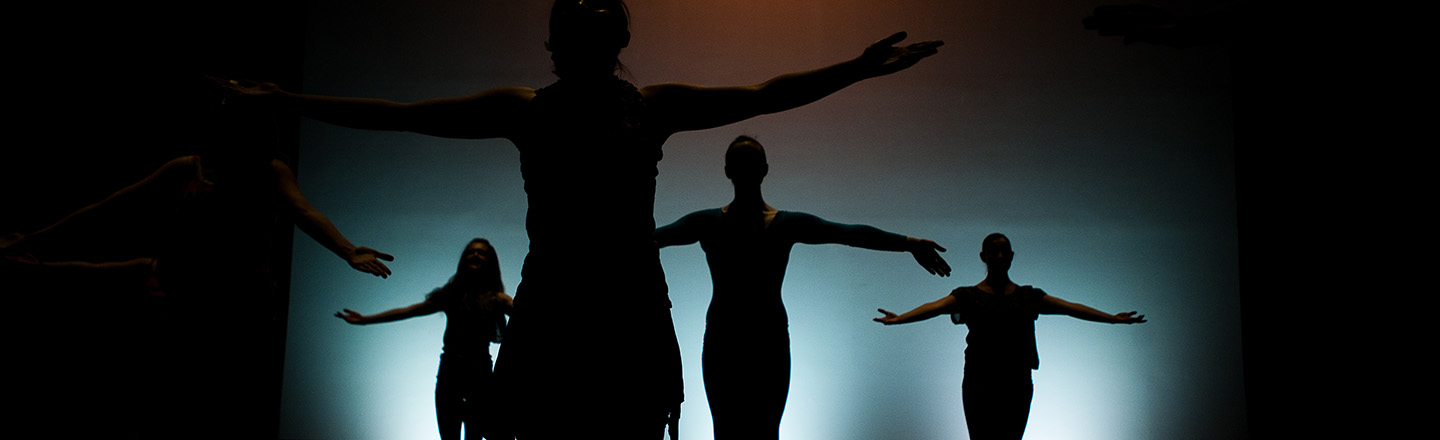 A row of 8 evenly spaced dancers with bright white windows in the background.