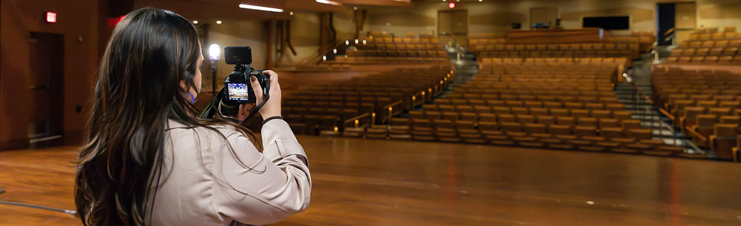 Women with camera standing on stage at the Martin Woldson Theater
