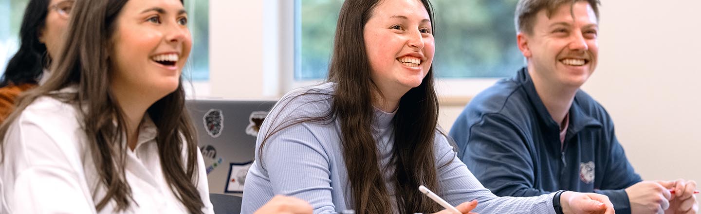 Graduate Accounting Students Smiling at Desks in Class