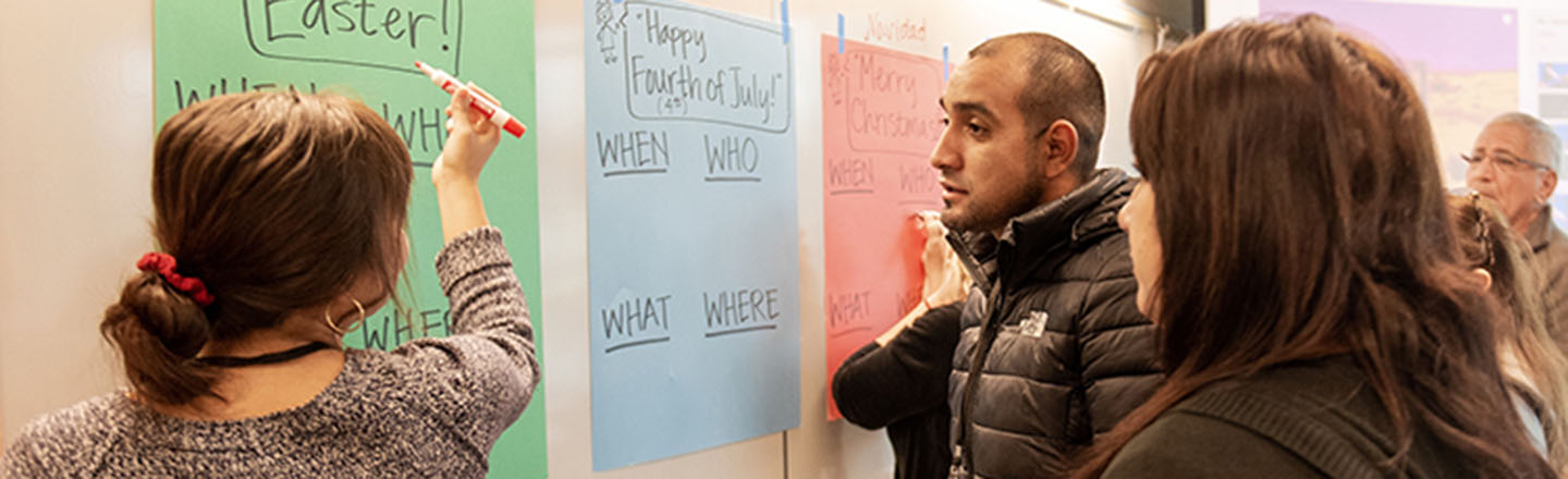 Students writing on colored paper on a white board