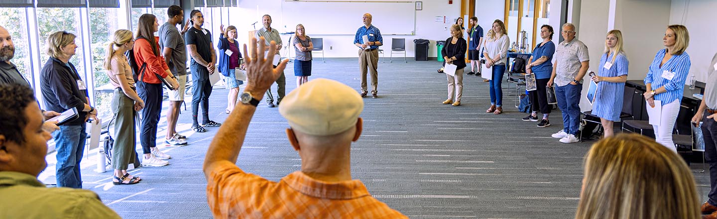 Person raising hand in a group of people standing in a circle in a classroom
