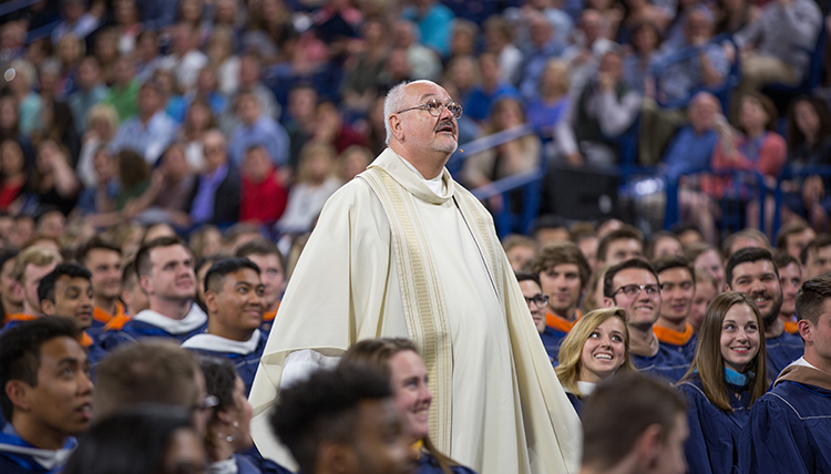 Father Brad Reynolds stands amid crowd of graduates during homily