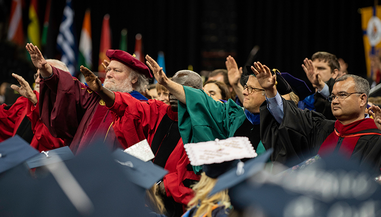jesuits and professors raise hands to bless graduates