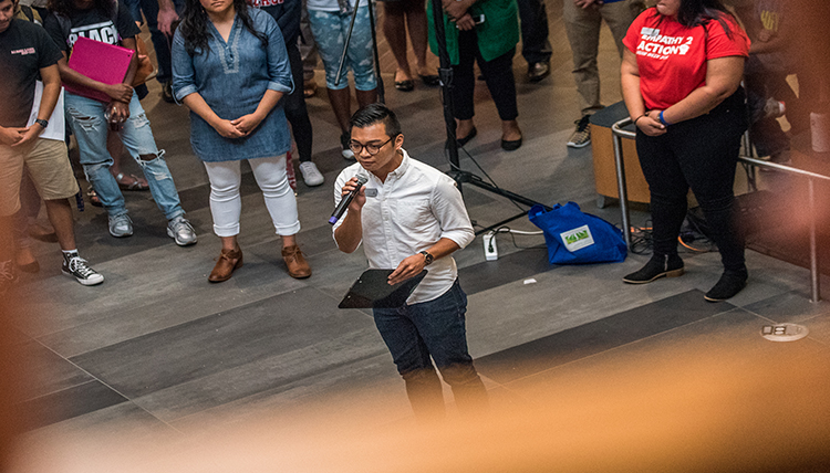 Carlo Juntilla surrounded by group in Hemmingson Rotunda while he gives a speech