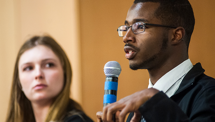 Caleb Dawson speaking into microphone while another student looks on