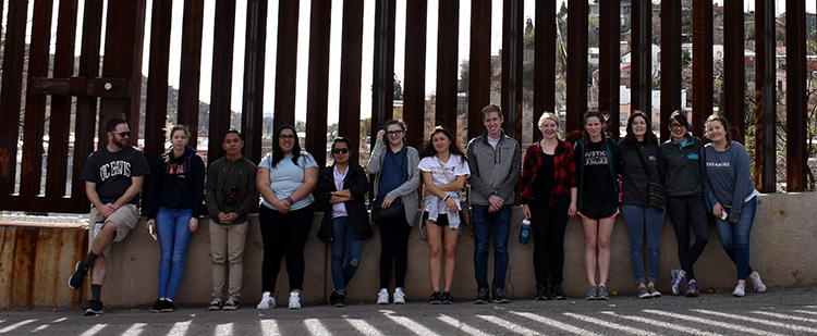Students stand for a picture in front of the border wall near Nogales