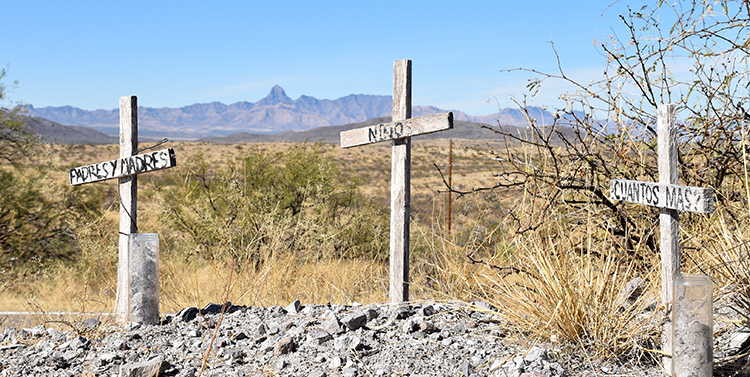 Three commemorative grave markers that read 'Padres y Madres', 'Niños', and '¿Cuantos mas?'
