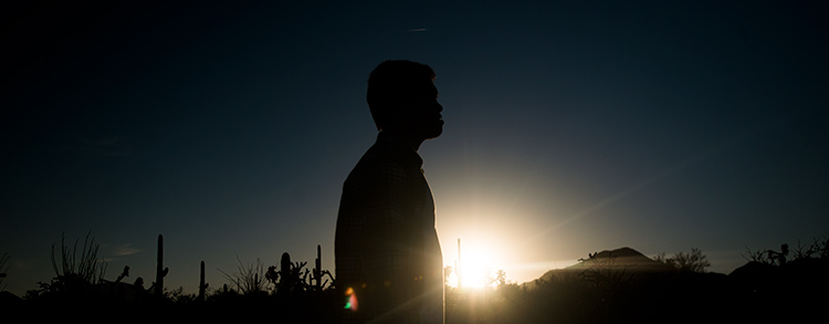 A student stands silhouetted against the sun