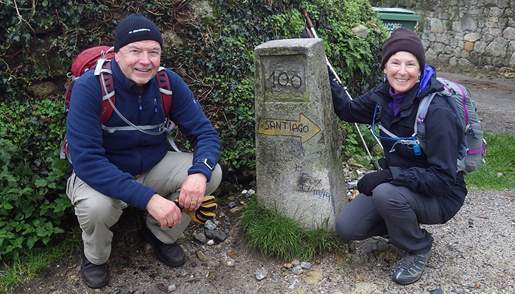 a couple kneels beside a mile marker on the Camino de Santiago