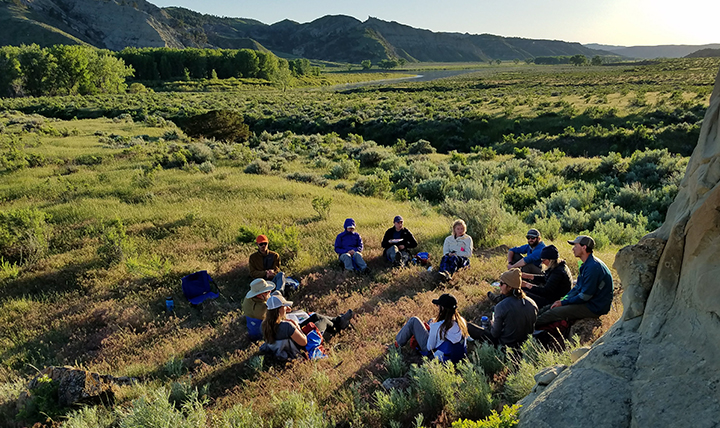 Group of students sit in a circle in a field at dusk