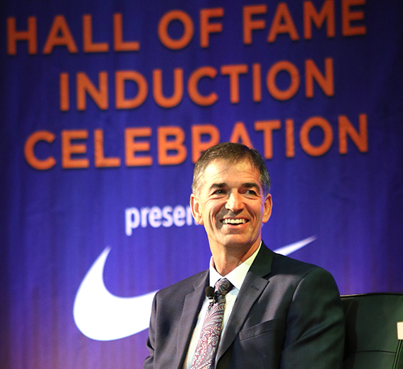 John Stockton smiling in front of a banner that denotes his induction into the Basketball Hall of Fame