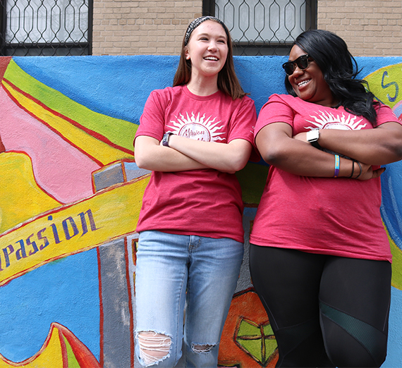 Two girls smile and pose in front of a colorful mural outside a nonprofit in New York City.  