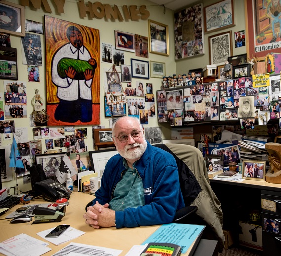 Father Greg Boyle sits in his picture and painting filled office. 