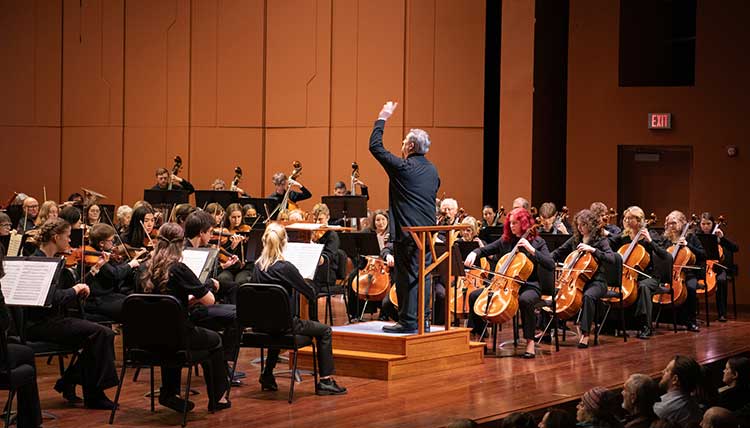Full orchestra with conductor on a large stage.