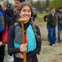 Smiling student wearing a blue life vest and holding a boat paddle.