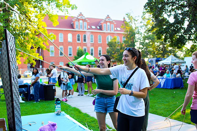 Two people playing a game near a large vertical board on a grassy surface.