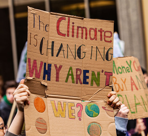 A colorful cardboard placard is viewed close up, saying the climate is changing, why aren't we, in the hands of ecological activists as they protest in the city
