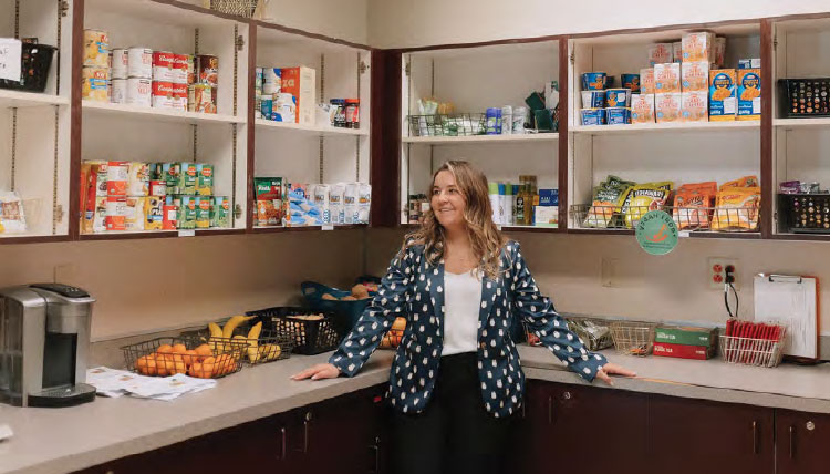 A woman stands in a pantry filled with assorted groceries.