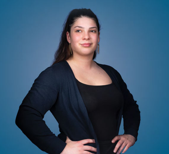 A woman with a confident stance against a blue background.