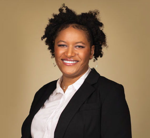 A joyful woman with curly hair wearing a white shirt and black blazer against a beige backdrop.