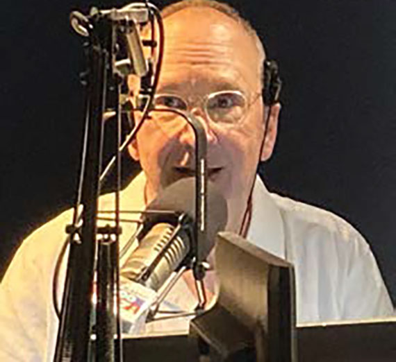 Gregg Hersholt sits behind a radio microphone. 