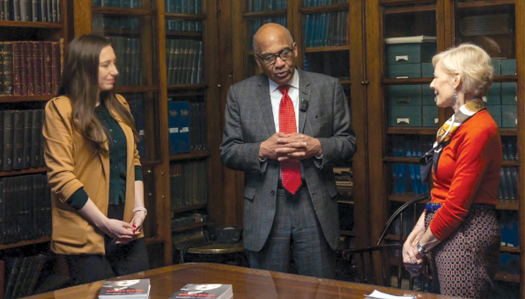 two woman with a man and books