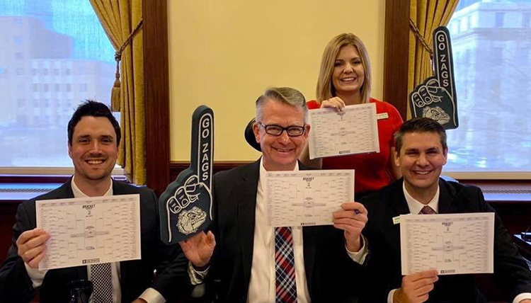 three alumni in ID Governors office show their March Madness brackets and Go Zags materials