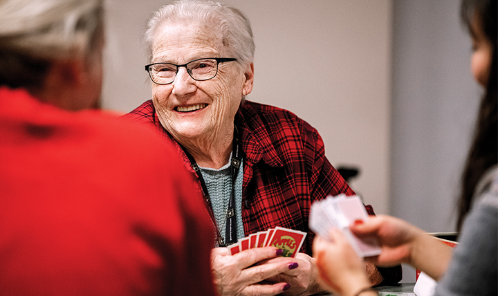 An elderly woman plays a card game with students. 