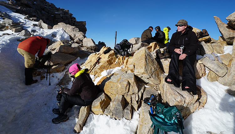 hikers take a rest break on rocks in the snow on the mountain