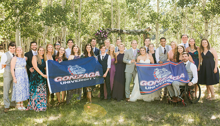 A group of wedding guests standing outside, holding two Gonzaga University flags.