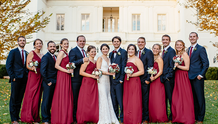 large wedding party in crimson attire outside mansion