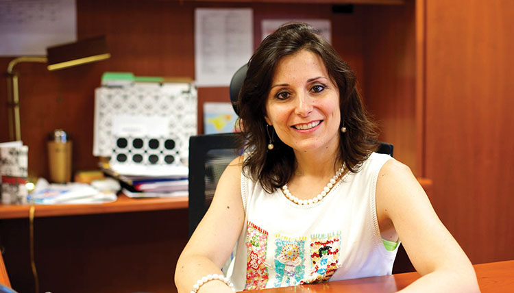 President Passerini smiling with her arms rested on a desk