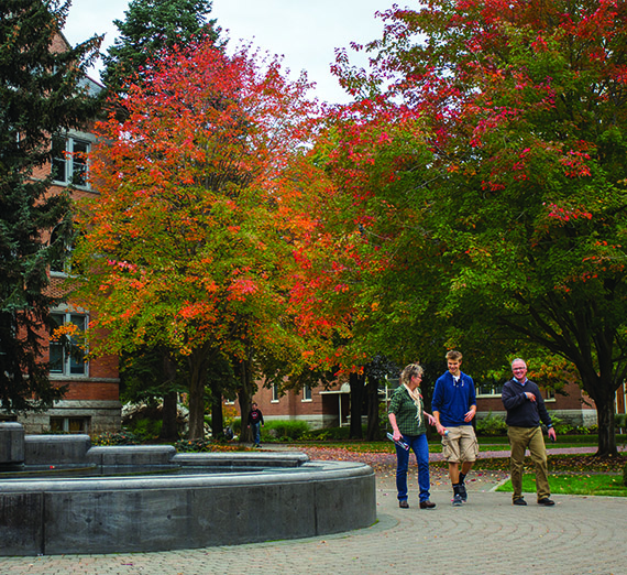 A family walks in front of a brick building with colorful trees around them.