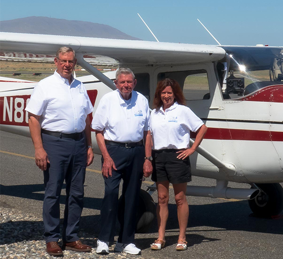 3 people standing by a small airplane