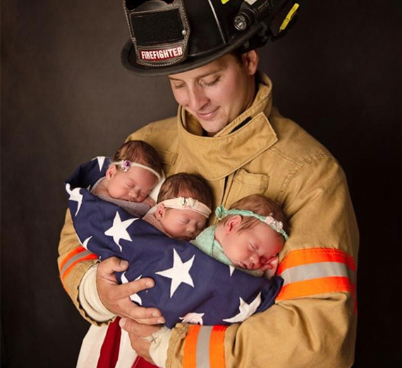 man in fireman uniform holding 3 babies in a flag