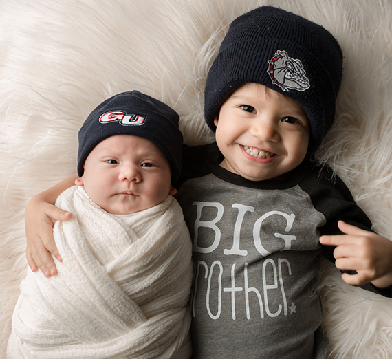 Baby asleep with a tennis ball with a Zag logo on it.